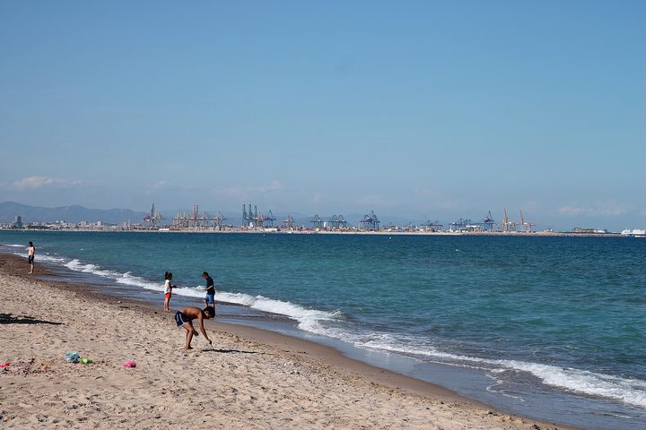 A wide sandy beach curving towards the Valencia skyline in the distance