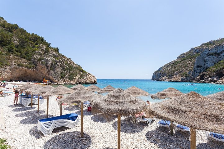 A turquoise cove of straw parasols and loungers below wooded cliffs