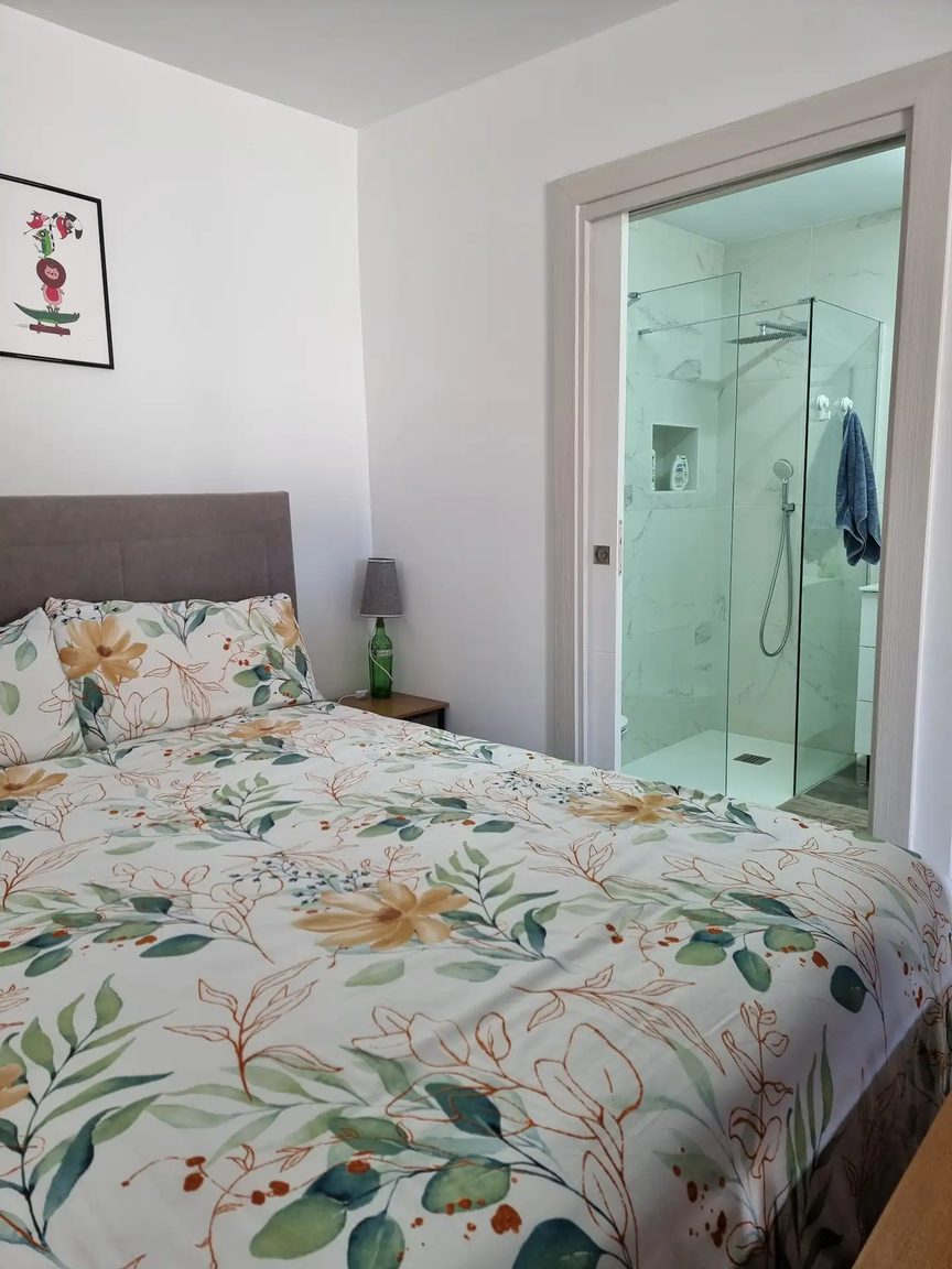 A bed with floral linen beside an open door to a glass walk in shower