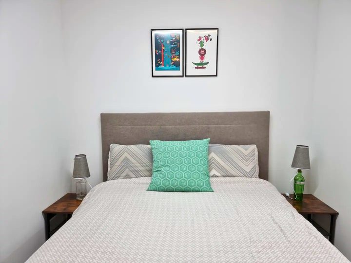 A double bed with a grey upholstered headboard, patterned cushions and framed prints above