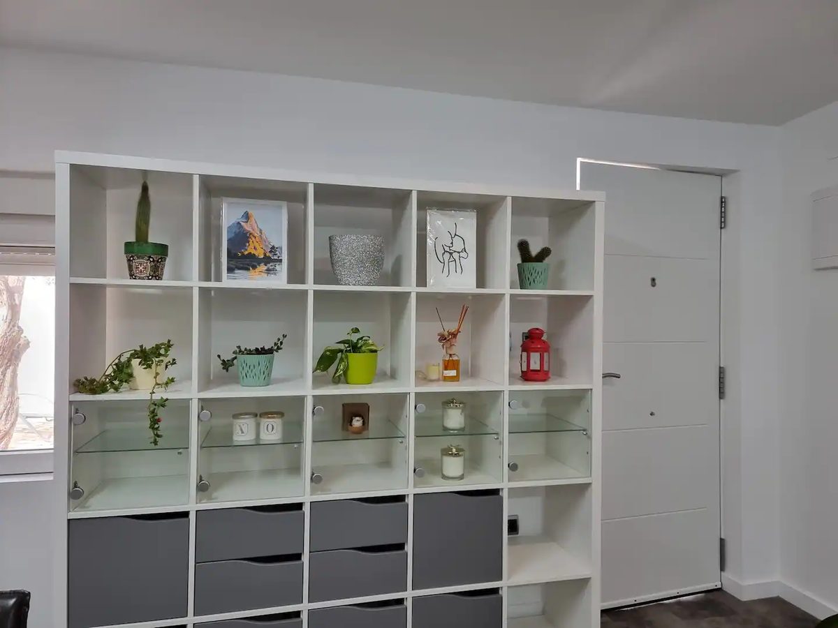 A white shelving unit holding plants, books and candles beside the studio door
